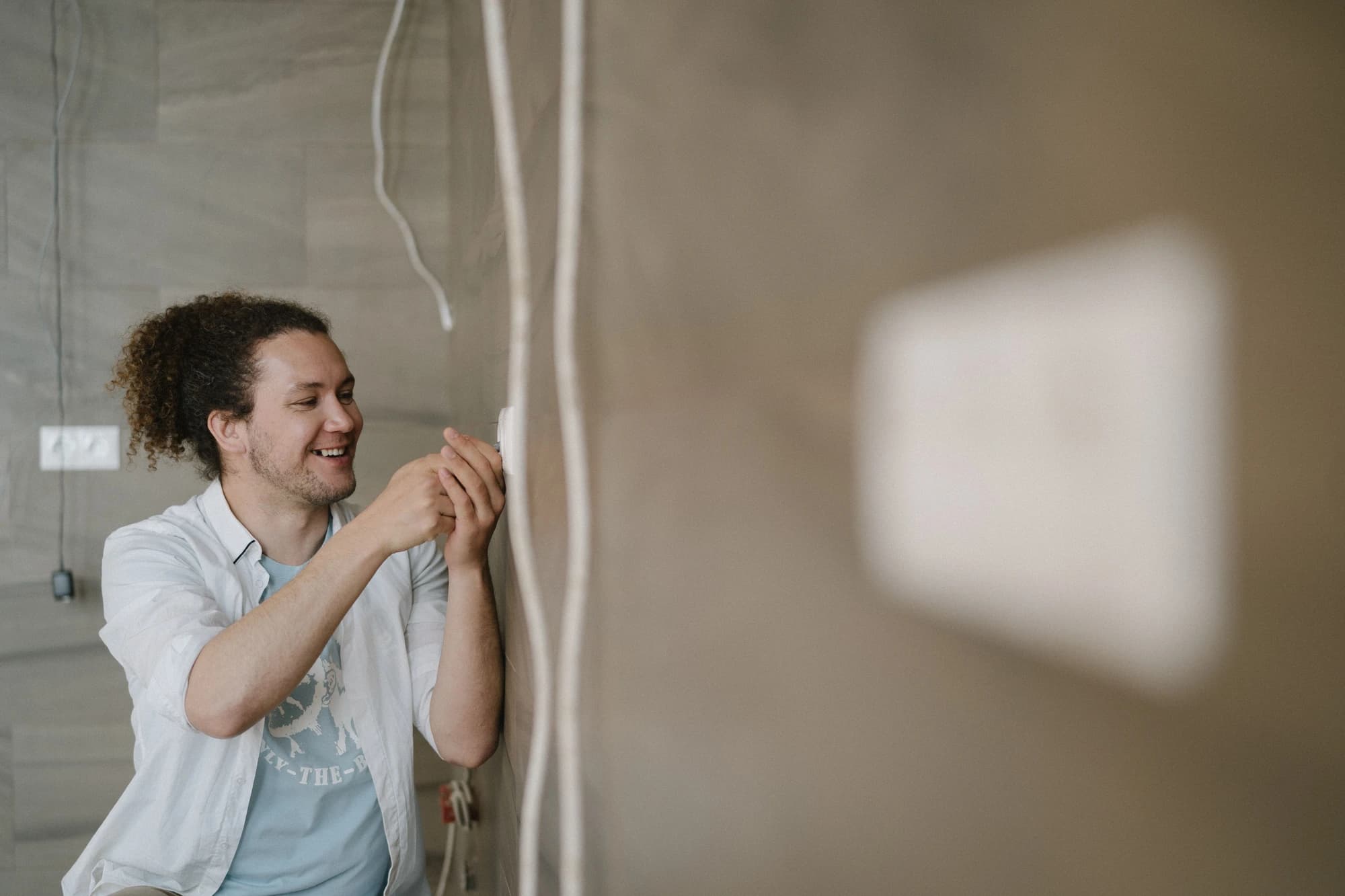 Un électricien souriant installe une prise murale dans un logement